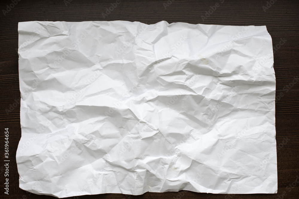 White crumpled paper on a dark wooden background. White crumpled paper on a dark wooden background.