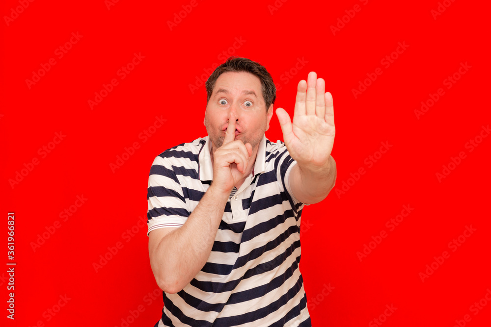 Fototapeta premium Glad mysterious male bee belly model shows silence sign or hush gesture.red background