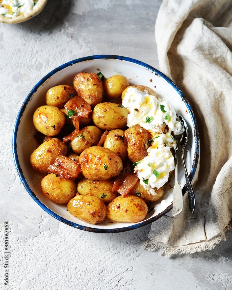 Baked young potatoes with bacon and sour cream sauce on a gray background, still life Baked young potatoes with bacon and sour cream sauce on a gray background, still life