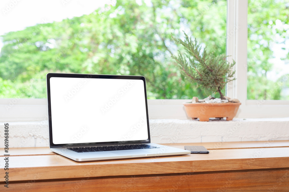 A beautiful blank screen laptop on a wooden table at house. a view form window is a tree, technology and nature concept A beautiful blank screen laptop on a wooden table at house. a view form window is a tree, technology and nature concept