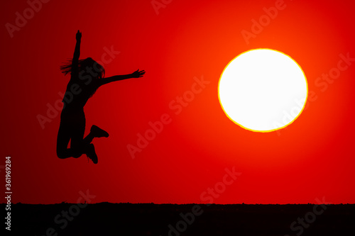 Young girl jumps high in joy. At sunset, the silhouette of his body is visible. The concept of nature and beauty. Orange sunset. Girl silhuette at sunset.