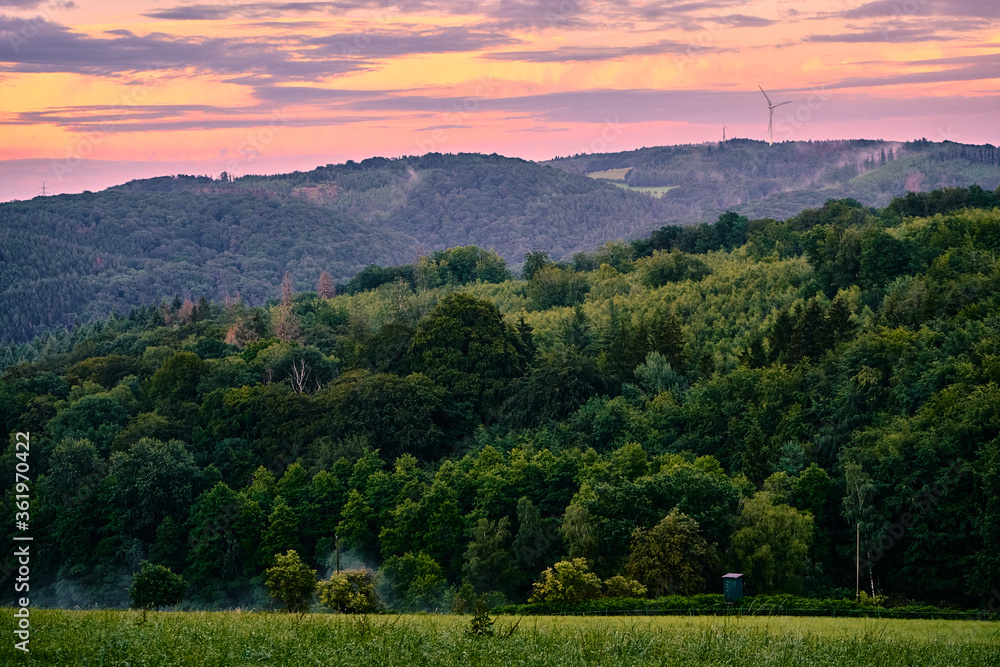 Afterglow over a wooded hilly landscape.