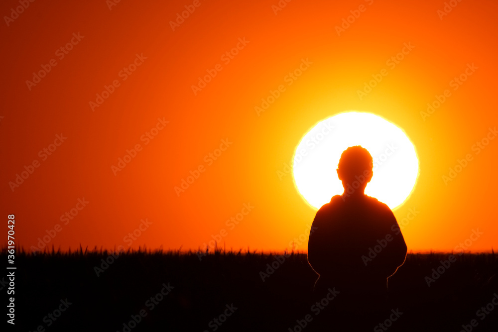 A little girl stands on the meadow and watches the beautiful sunset. close up of sun big, sky orange color.