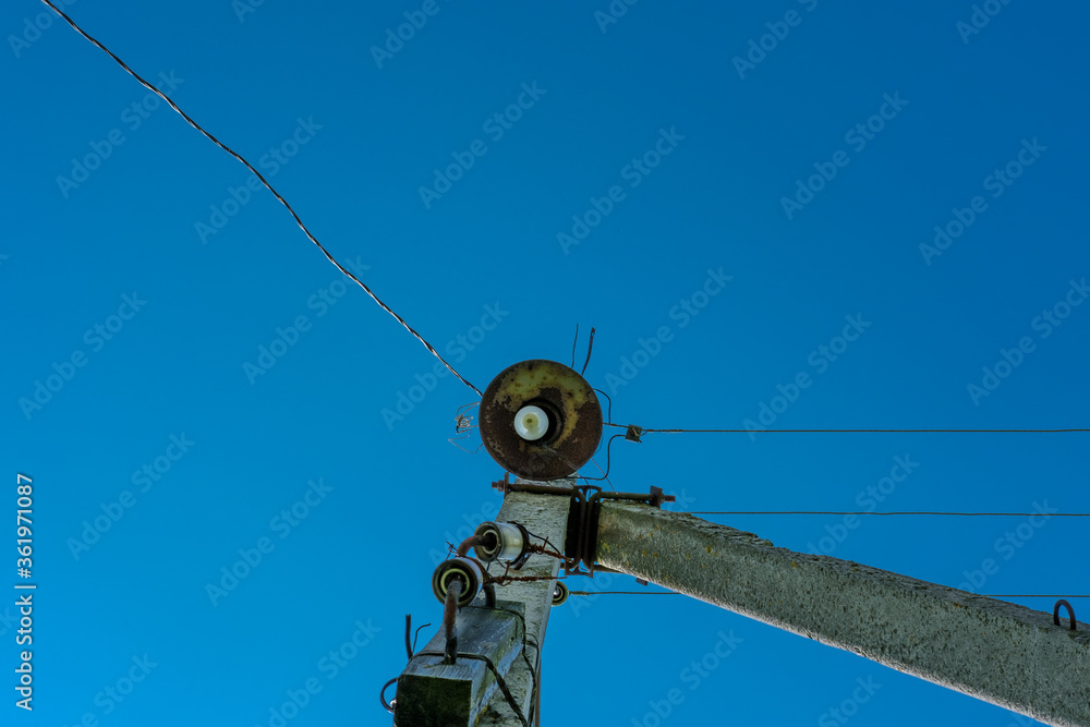 Obraz premium Old rusty lantern on an electric pole with wires, against a clear blue sky.