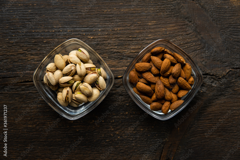 Almond and pistachio in a small plates which standing on a vintage wooden table. Nuts is a healthy vegetarian protein and nutritious food. Almond and pistachio in a small plates which standing on a vintage wooden table. Nuts is a healthy vegetarian protein and nutritious food.