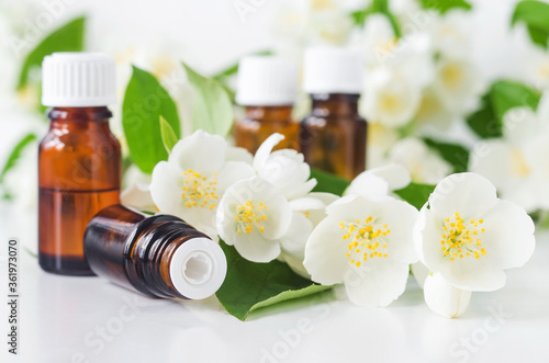 Small glass bottle with essential jasmine oil  tincture  infusion  perfume  on the white background. Jasmine flowers close up. Aromatherapy  spa and herbal medicine ingredients. Copy space.