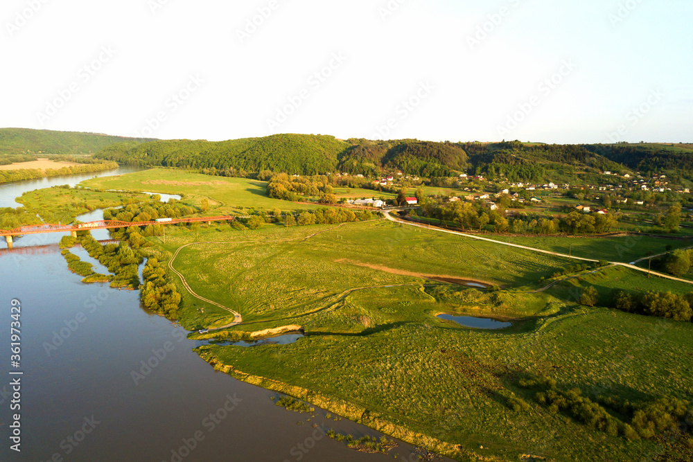 Aerial view of bright river flowing through green meadows in spring.