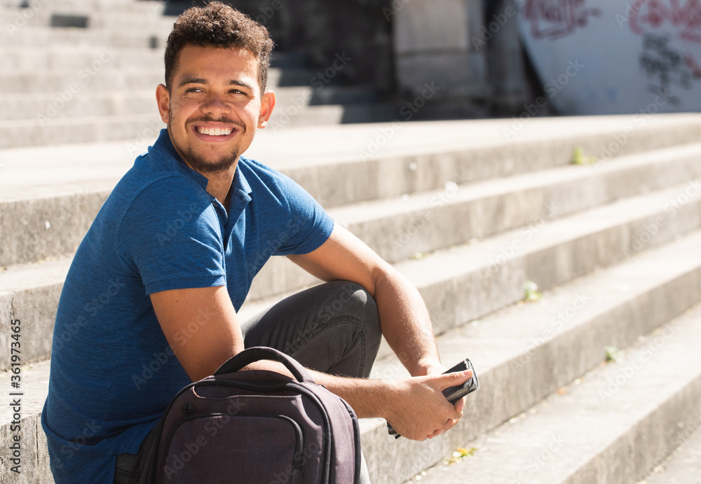 Close up side of smiling young african american man sitting outside on steps holding phone