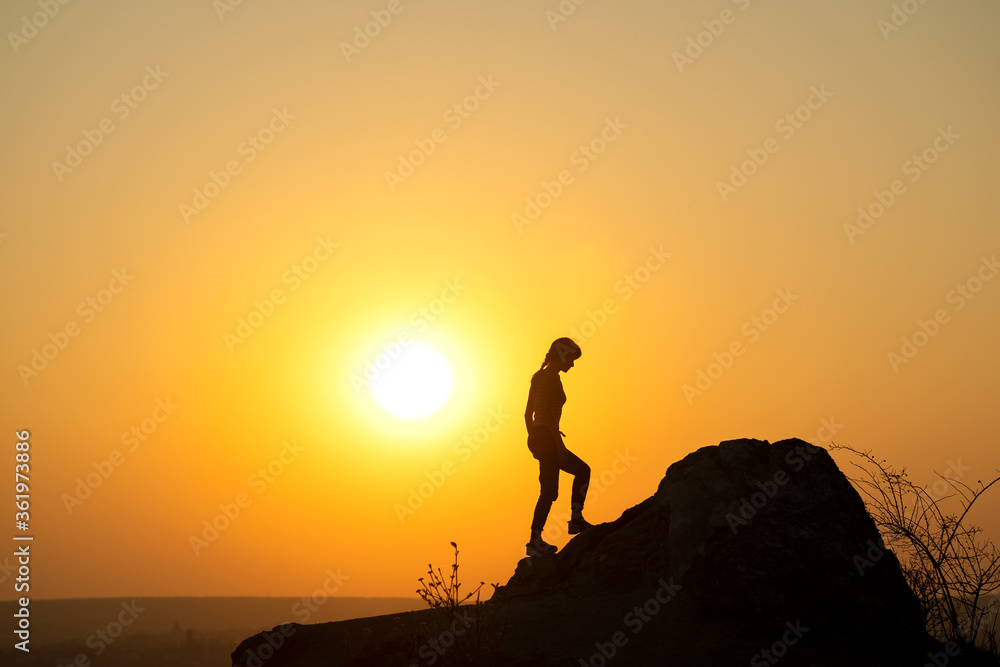 Silhouette of a woman hiker climbing up a big stone at sunset in mountains. Female tourist on high rock in evening nature. Tourism, traveling and healthy lifestyle concept.