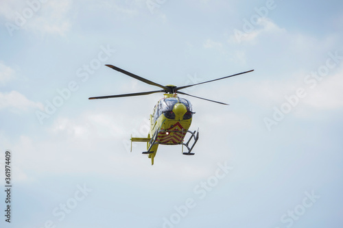 The air ambulance, service arrives at the scene of an accident. Flying yellow medical ambulance helicopter. Background of blue sky with clouds. Pest county / Hungary - 06/01/2020
