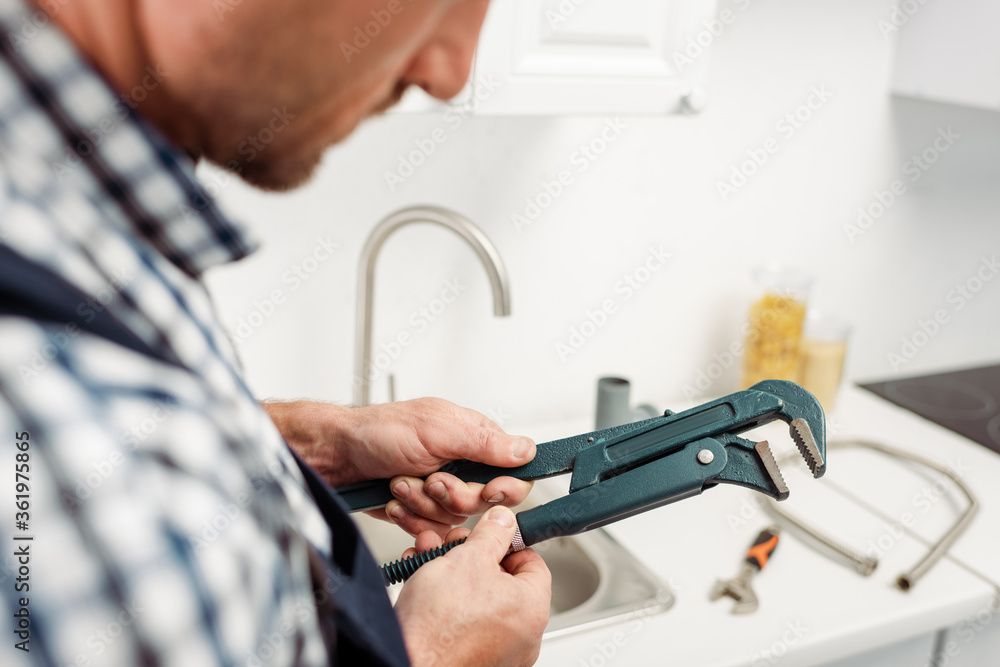 Cropped view of plumber holding pipe wrench in kitchen