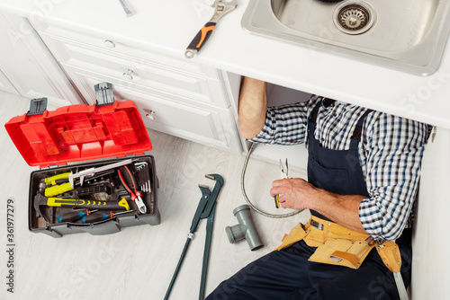 High angle view of plumber fixing kitchen sink with pliers near instruments and toolbox on floor