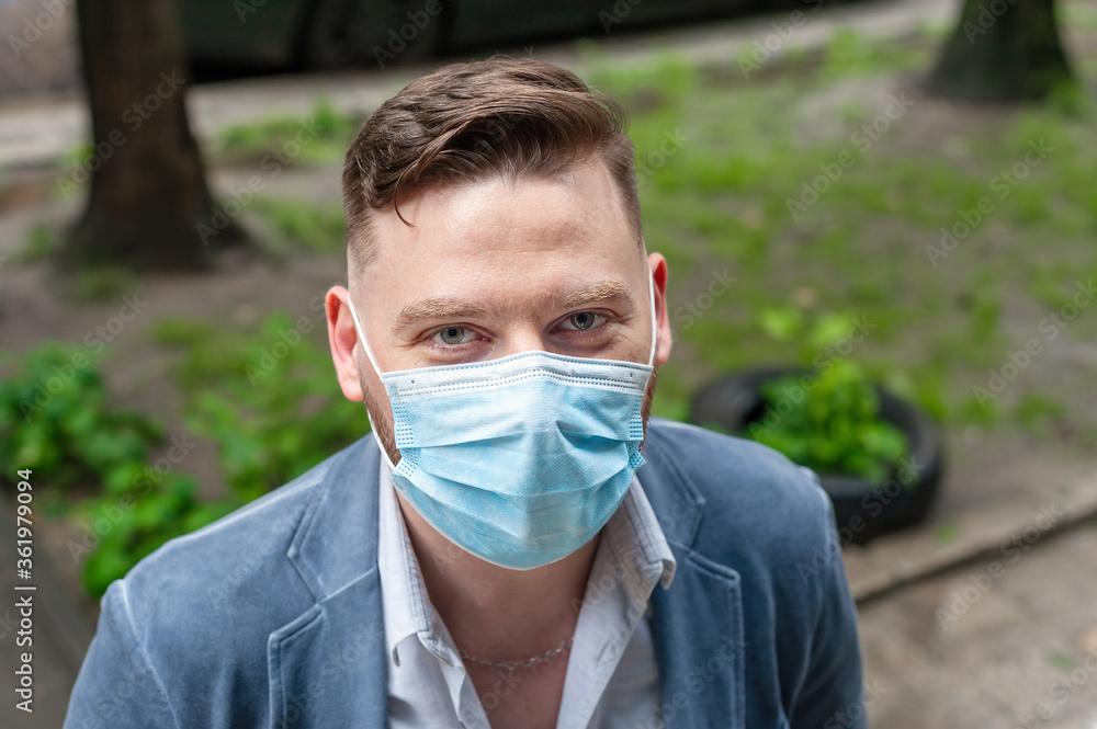 Caucasian man in disposable blue medical face mask on the street. Close-up. He is looking at the camera. Coronavirus protection. Caucasian man in disposable blue medical face mask on the street. Close-up. He is looking at the camera. Coronavirus protection.
