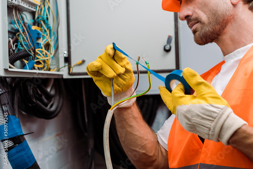 Foto Cropped view of electrician using insulating tape while fixing wires of electric