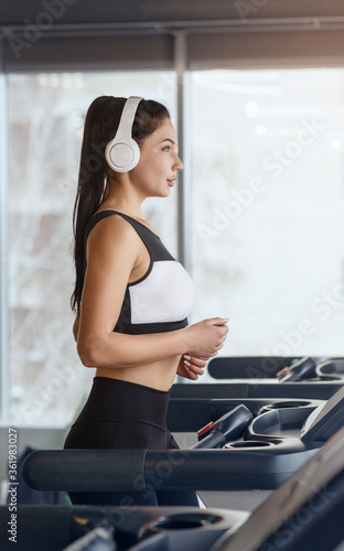 Sportive girl in headset enjoying music while running on treadmill at health club