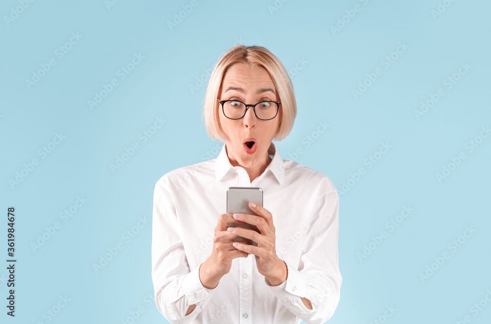 Shocked business lady shouting OMG while looking at smartphone against blue background Shocked business lady shouting OMG while looking at smartphone against blue background