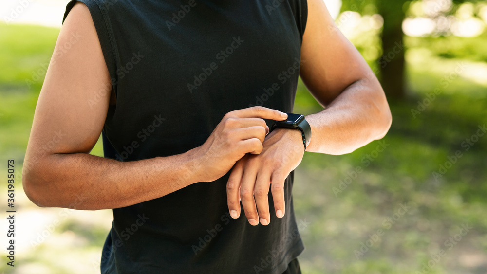 Closeup view of young guy checking his smartwatch or fitness tracker during training outdoors