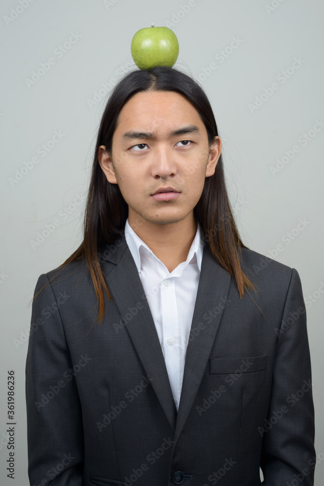Young Asian businessman with long hair looking at apple on top of head Young Asian businessman with long hair looking at apple on top of head