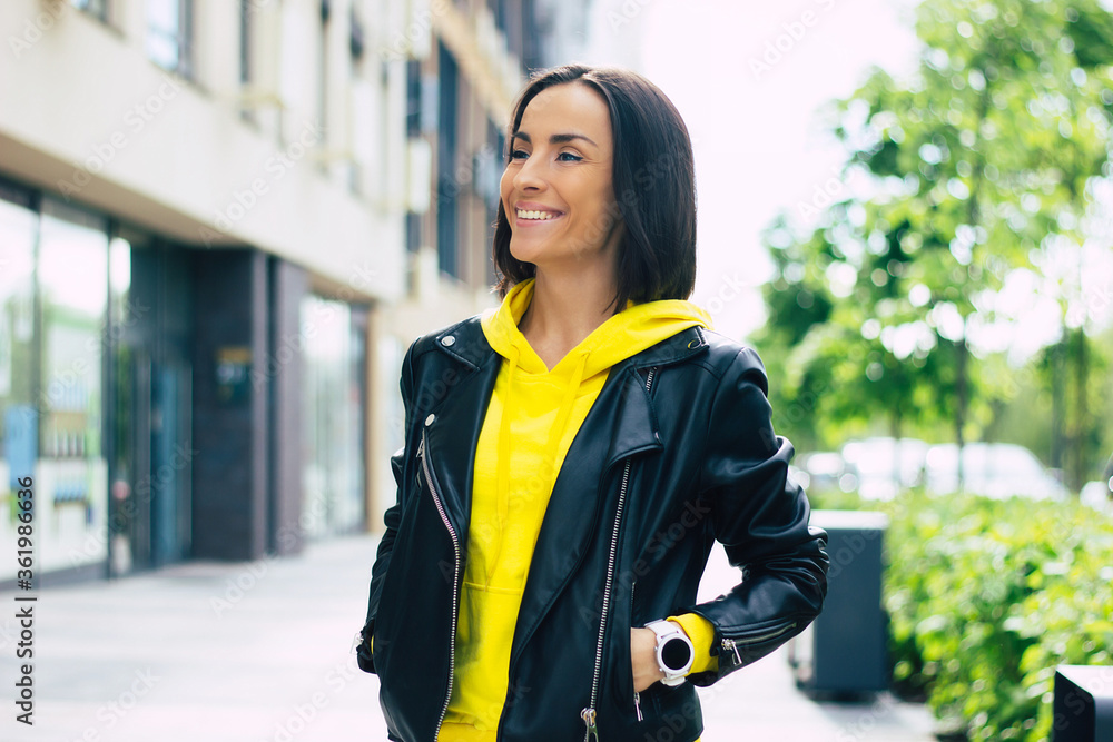 Good walk with my smartwatch! A half-length photo of a young woman, dressed in leather jacket and yellow hoodie, enjoying her walk with her new smartwatch.