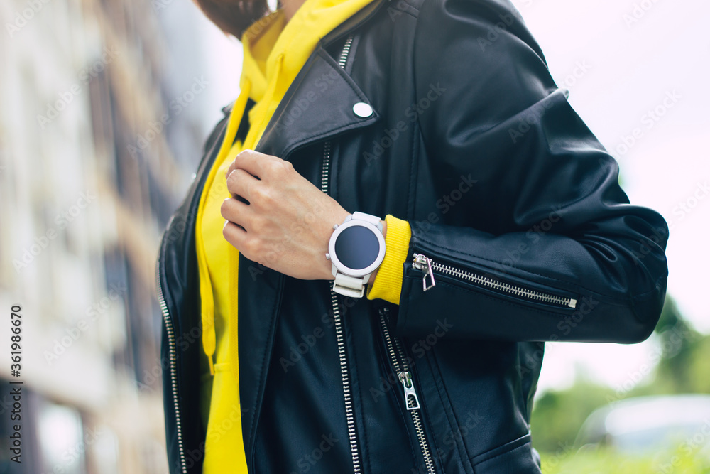 My new smartwatch! A half-length photo of a young woman's look, that consists of her new powerful, modern smartwatch, leather jacket and yellow hoodie.