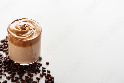 delicious Dalgona coffee in glass near coffee beans on white background