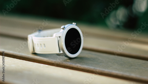 White smartwatch. A close-up photo of a white, stylish, modern smartwatch, lying on the wooden bench.