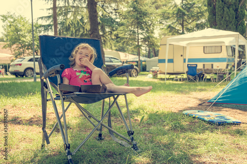 Cute blonde girl sitting at the table in camping resort.