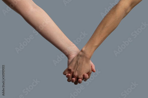Close-up of light-skinned and dark-skinned people holding hands