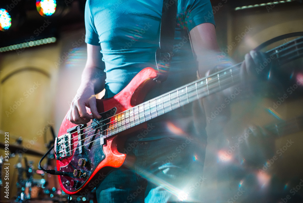 Obraz premium The musician plays the electric bass guitar on stage. Guitar neck close-up on a concert of rock music in the hands of a musician. Fingers on fretboard