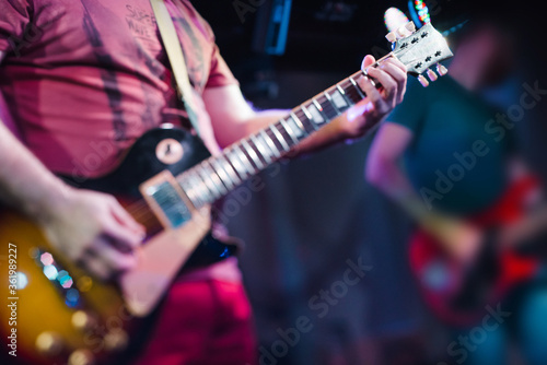 The musician plays the electric guitar on stage. Guitar neck close-up on a concert of rock music in the hands of a musician. Fingers on fretboard