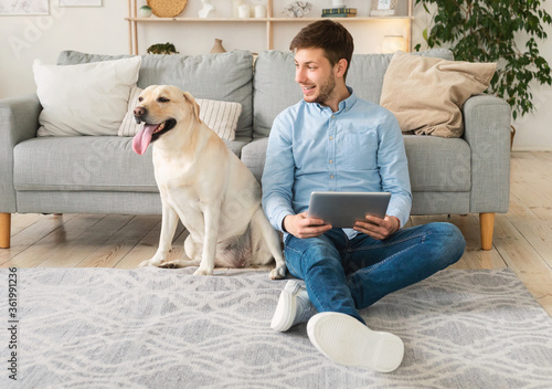 Young man at home with a tablet and labrador