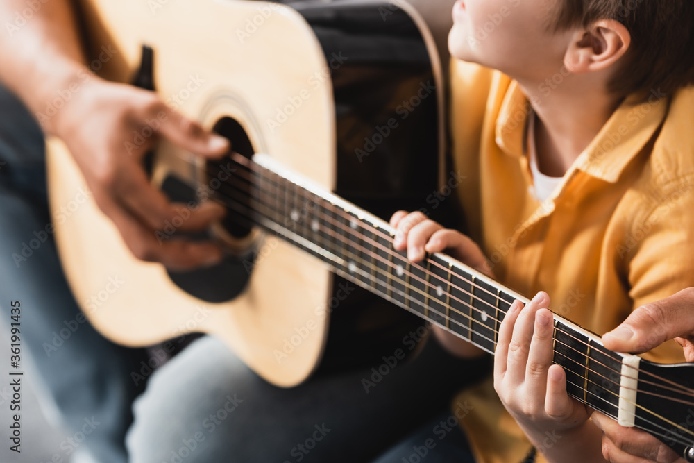 cropped view of father teaching son how to play acoustic guitar, selective focus