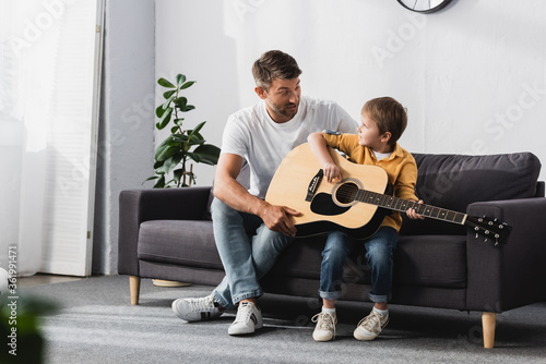 father and son looking at each other while boy learning how to play acoustic guitar