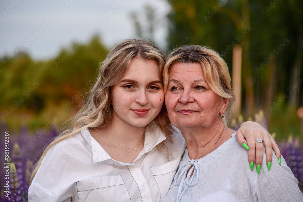 A grandmother and a teenage granddaughter pose in lupine fields. A grandmother and a teenage granddaughter pose in lupine fields.
