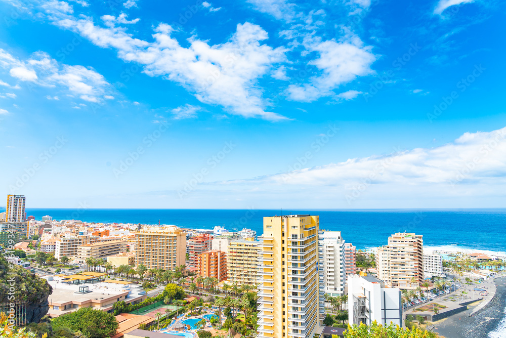Landscape of the city by the ocean with a blue ske with clouds. Puerto de La Cruz on a sunny day. Tenerife, Spain