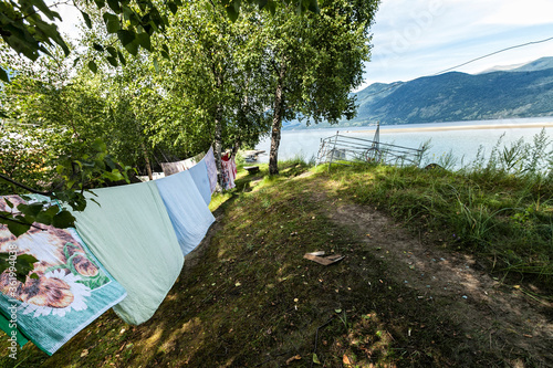 bedding is dried on a rope by the lake in the mountains, an old grave on the edge of a cliff, green trees with dense foliage