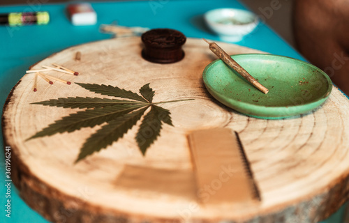 Fototapeta Naklejka Na Ścianę i Meble -  Grinder with cannabis joint, dry leaf of weed on wooden table - Focus on pipe filter