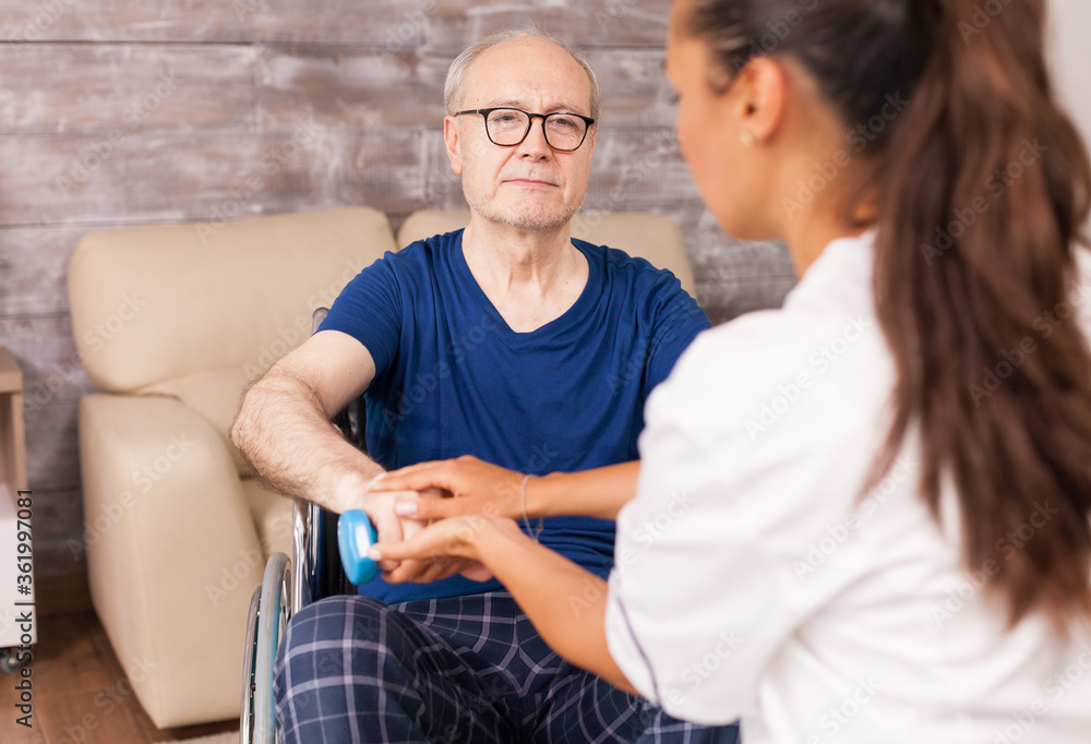 Obraz premium Caregiver helping paralyzed man to recover using dumbbells for the arms muscles. Disabled handicapped old person with social worker in recovery support therapy physiotherapy healthcare system nursing