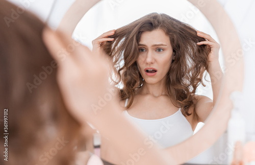 Фотография Shocked young woman holding her hair, looking at mirror