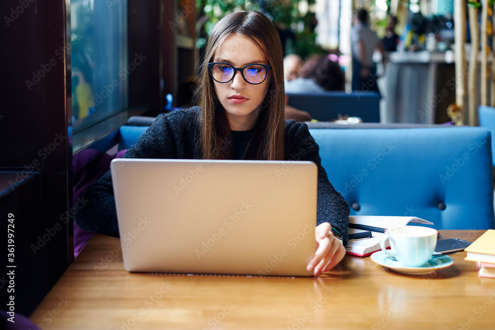 Pensive brunette copywriter in eyewear searching information in network for publication working on freelance, smart female student watching training webinar improving knowledge during free time