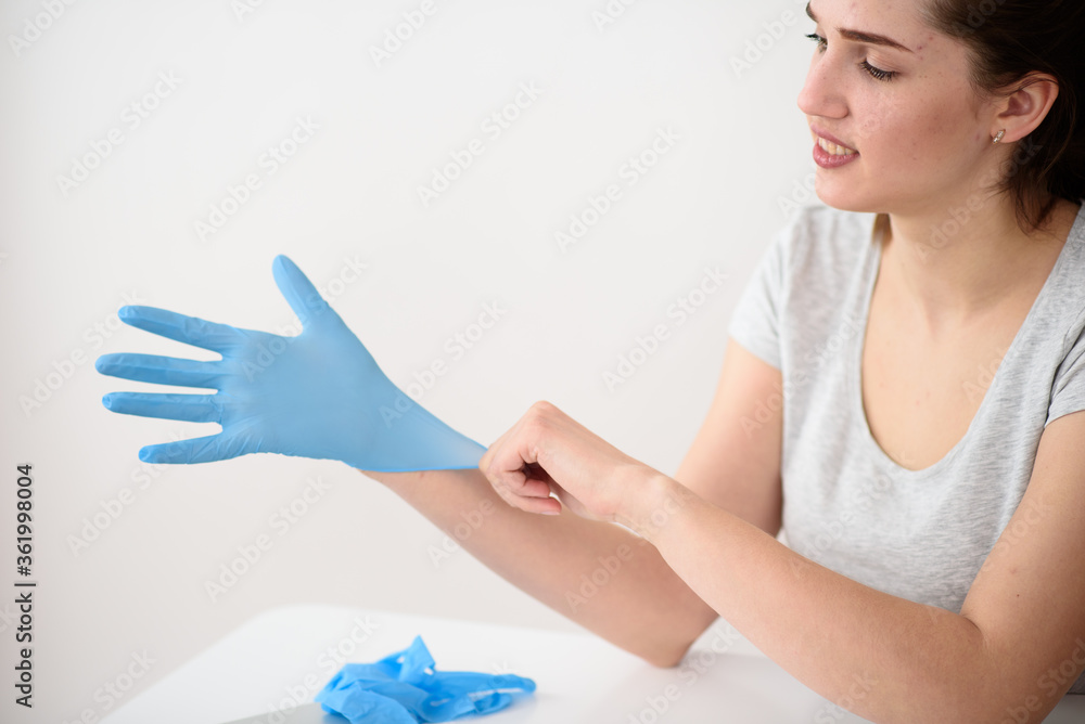 Girl wears rubber gloves before work sitting at a table on a light background Girl wears rubber gloves before work sitting at a table on a light background
