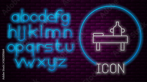 Glowing neon line Massage table with oil icon isolated on brick wall background. Neon light alphabet. Vector.