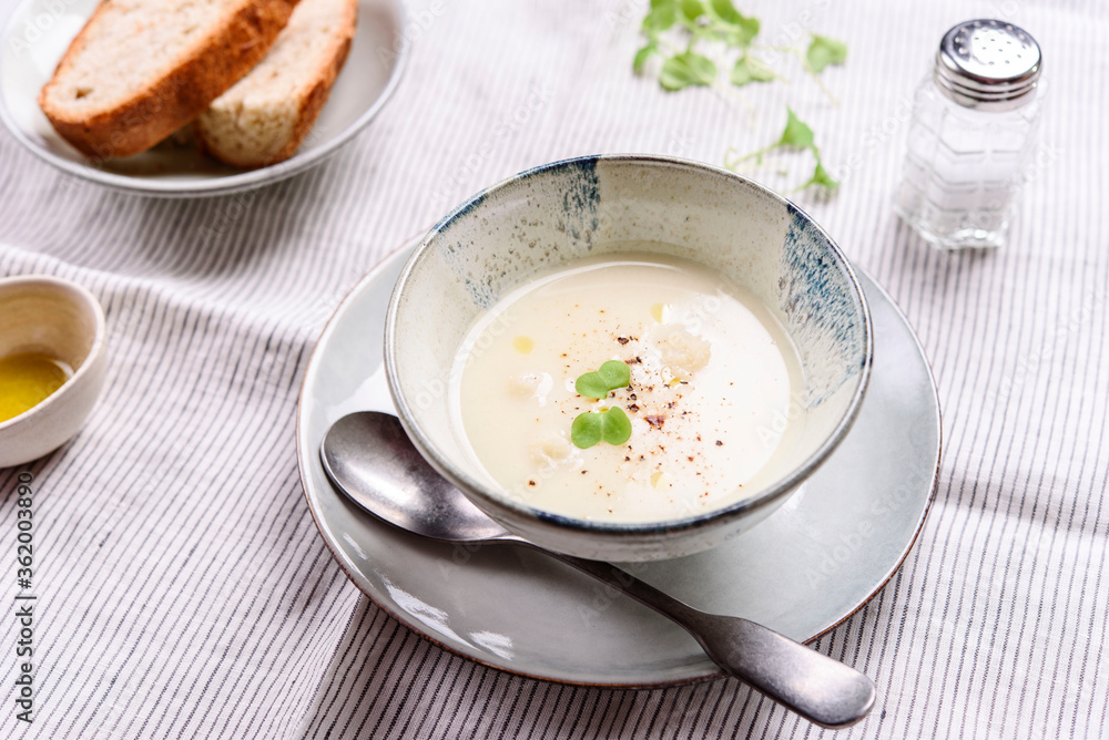 Cauliflower and Potato Cream Soup served with herbs and pepper on white linen striped tablecloth. Selective focus Cauliflower and Potato Cream Soup served with herbs and pepper on white linen striped tablecloth. Selective focus