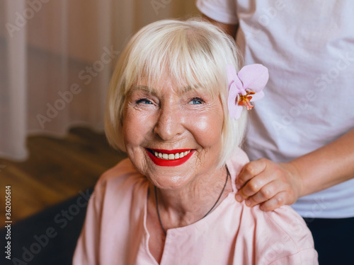 elderly (old) caucasian stylish woman with gray hair and pink phalaenopsis in her hair sitting at thai massage. Anti age, healthy lifestyle, travel, thai massage concept