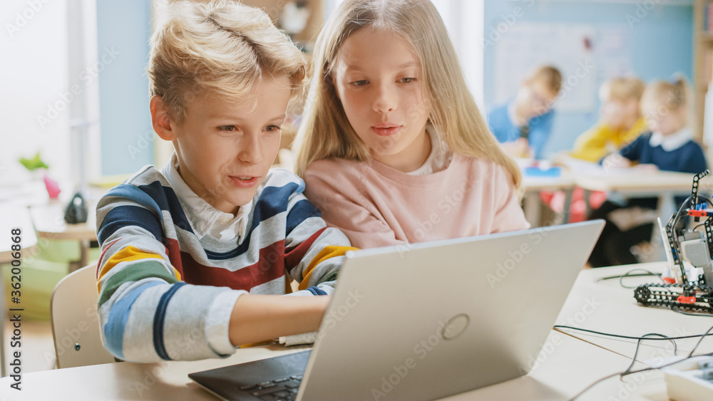 Brilliant Schoolgirl and Schoolboy Talk and Use Laptop to Program Software for Robotics Engineering Class. Elementary School Science Classroom with Children Working on Technology. STEM Education Brilliant Schoolgirl and Schoolboy Talk and Use Laptop to Program Software for Robotics Engineering Class. Elementary School Science Classroom with Children Working on Technology. STEM Education