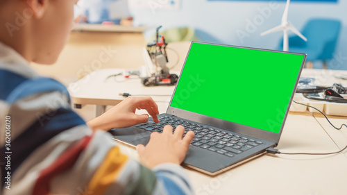 Elementary School Computer Science Classroom: Over the Shoulder View of a Kid Using Green Chroma Key Screen Laptop to Program Software for Robotics Engineering Class