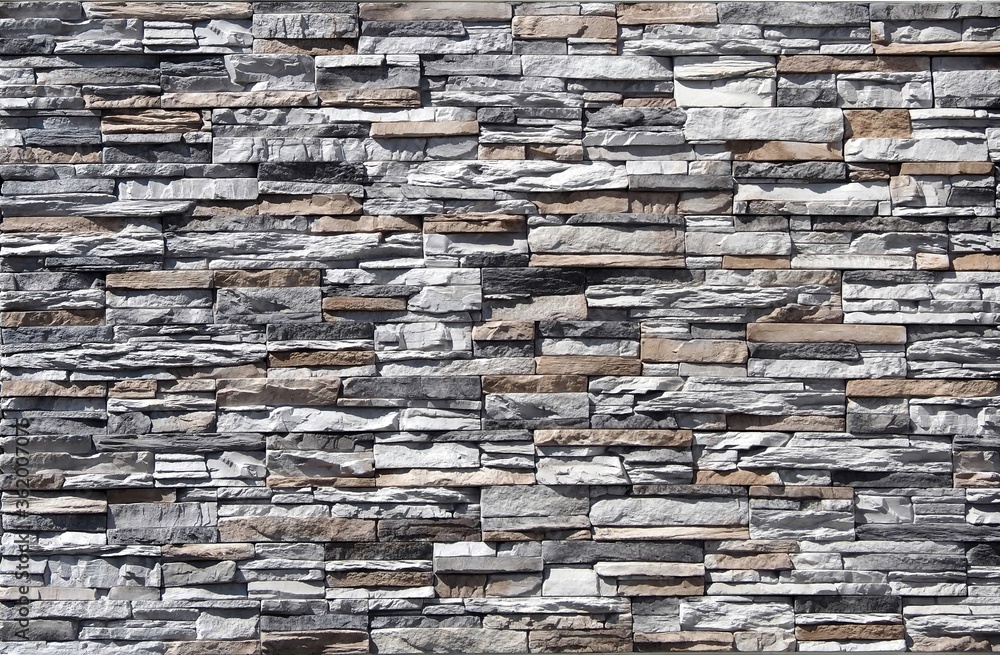 Stone cladding wall made of  striped stacked embossed natural rocks. Colors are gray, black, brown and white. 