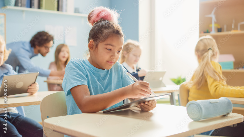 Elementary School Computer Science Class: Cute Girl Uses Digital Tablet Computer, Her Classmates work with Laptops too. Children Getting Modern Education in STEM, Playing and Learning Elementary School Computer Science Class: Cute Girl Uses Digital Tablet Computer, Her Classmates work with Laptops too. Children Getting Modern Education in STEM, Playing and Learning