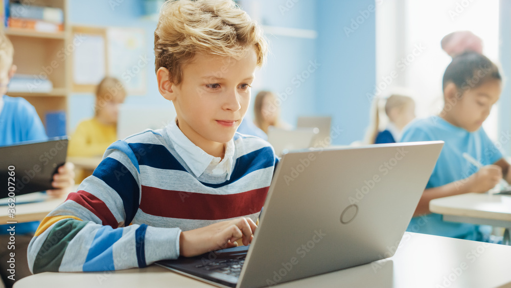 Elementary School Computer Science Class: Smart Boy Uses Laptop Computer, His Classmates work with Laptops too. Children Getting Modern Education in STEM, Playing and Learning Elementary School Computer Science Class: Smart Boy Uses Laptop Computer, His Classmates work with Laptops too. Children Getting Modern Education in STEM, Playing and Learning