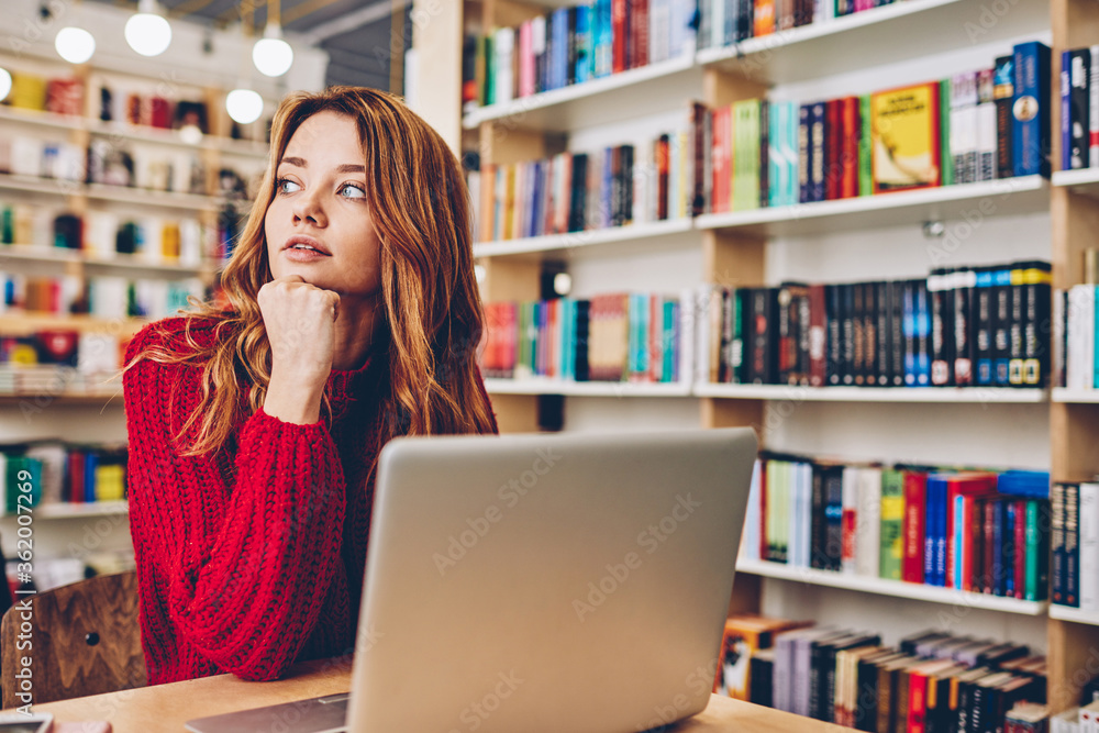Contemplative skilled hipster girl pondering on information taking at bookstore from modern laptop computer, caucasian pensive woman sitting at desktop with netbook and thoughtful looking away Contemplative skilled hipster girl pondering on information taking at bookstore from modern laptop computer, caucasian pensive woman sitting at desktop with netbook and thoughtful looking away